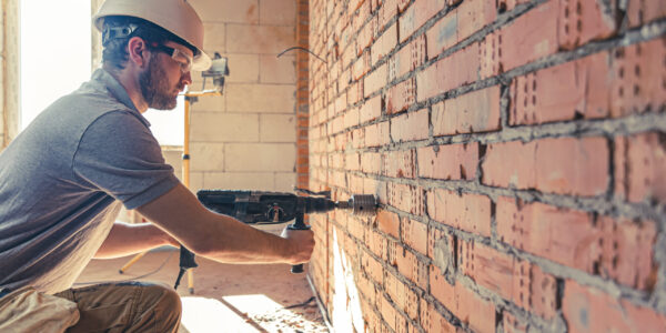 Handyman at a construction site in the process of drilling a wall with a perforator.